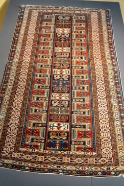 Farklı renkleri ve desenleri olan uzun bir halı. Halı masanın üstünde. Halı çok renkli ve çok detay içeriyor.