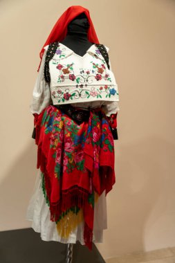 Çiçek desenli atkısı olan kırmızı beyaz elbiseli bir kadın. Atkı kırmızı ve sarı ve kalçalarına sarılı.