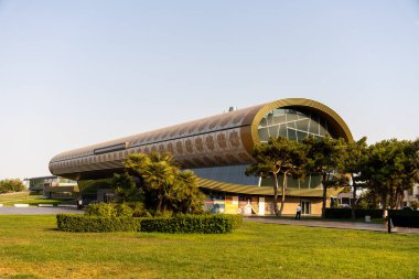 Kavisli çatısı ve bir sürü penceresi olan büyük bir bina. Bina ağaçlar ve otlarla çevrili.