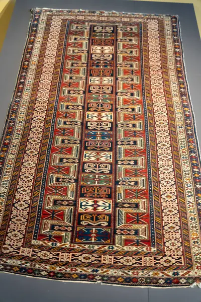 Farklı renkleri ve desenleri olan uzun bir halı. Halı masanın üstünde. Halı çok renkli ve çok detay içeriyor.