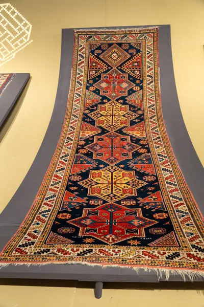 Üçgen şeklinde uzun mavi ve kırmızı bir halı. Halı bir müzede sergileniyor.