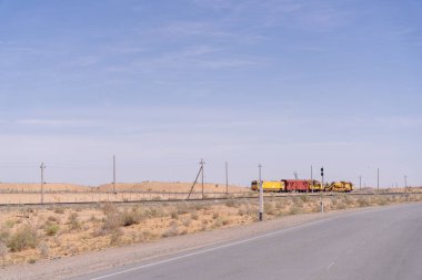 Çölde bir tren raylarda ilerliyor. Tren sarı ve kırmızıdır. Gökyüzü mavi ve berrak
