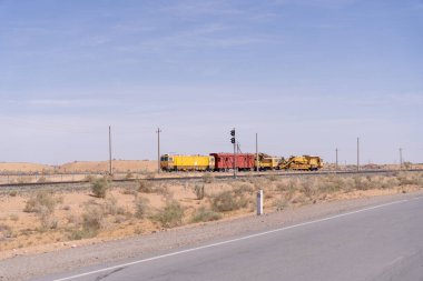 Çölde bir tren raylarda ilerliyor. Tren sarı ve kırmızıdır. Çöl kuru ve çoraktır.