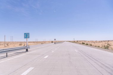 Yan tarafında mavi bir işaret olan uzun, boş bir otoyol. Gökyüzü açık ve mavi