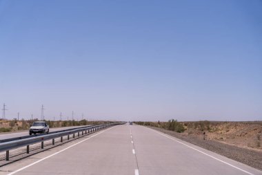 Üzerinde araba olan uzun, boş bir yol. Gökyüzü açık ve mavi. Yol geniş ve düz.