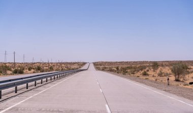 Arabasız ve insansız uzun bir yol. Gökyüzü açık ve mavi. Yol betondan yapılmış ve üzerinde beyaz çizgiler var.