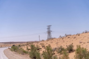 Uzakta bir elektrik hattı kulesi var ve gökyüzü açık ve mavi. Sahne huzurlu ve sakin, güç hattı kulesi çölün arka planında dik duruyor.