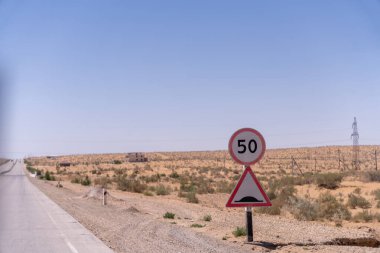 Üzerinde 50 yazan bir tabela olan bir yol. Yol boş ve gökyüzü mavi.