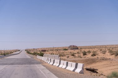 Yan tarafında beyaz çit olan bir yol. Gökyüzü mavi ve gökyüzünde uçan birkaç kuş var.