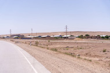 Arka planda birkaç ev olan bir yol. Evler küçük ve etrafta hiç insan yok.