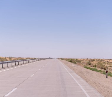 Üzerinde mavi bir gökyüzü olan uzun, boş bir yol. Yol uzun otlarla kaplı ve yolda bir kamyon var.