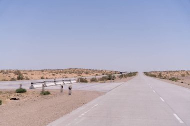 Uzakta birkaç çimento direği olan uzun, boş bir yol. Gökyüzü açık ve mavi