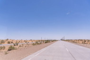 Üzerinde açık mavi gökyüzü olan bir yol. Yol boş ve üzerinde hiç araba yok.