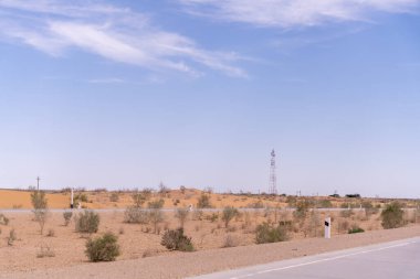 Ortasında telefon direği olan bir çöl manzarası. Gökyüzü açık ve mavi. Telefon direği uzundur ve sahnedeki tek nesnedir.