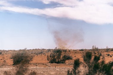 Çölde yerden büyük bir toz bulutu yükseliyor. Gökyüzü açık ve mavidir, birkaç bulut etrafa saçılmıştır. Manzara çorak ve çorak, sadece birkaç ağaç var.