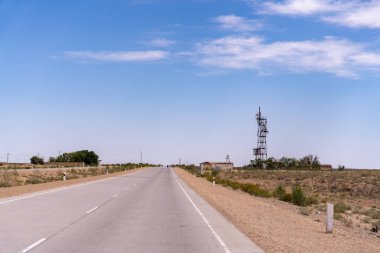 Arka planda uzun bir kule olan bir yol. Yol boş ve gökyüzü temiz.