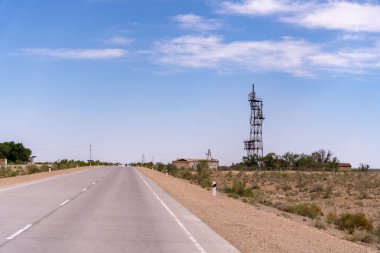 Arka planda uzun bir kule olan bir yol. Yol boş ve gökyüzü temiz.
