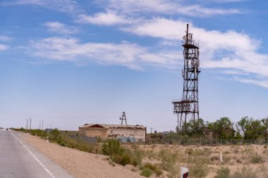 Çölün ortasında uzun bir kule var. Gökyüzü açık ve mavi. Kule çorak bir araziyle çevrilidir.