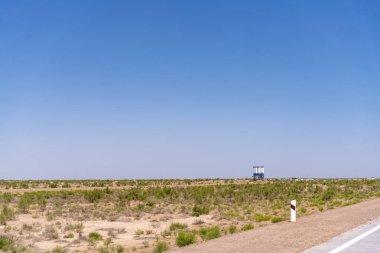 Arka planda mavi gökyüzü olan büyük boş bir alan. Yolun kenarında kırmızı ve beyaz bir tabela var.