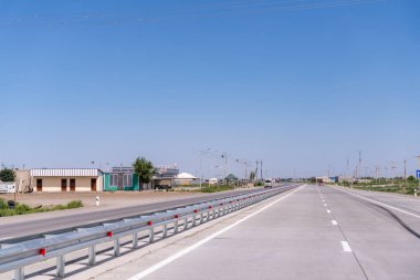 Arka planda birkaç bina olan uzun, boş bir yol. Gökyüzü açık ve mavi