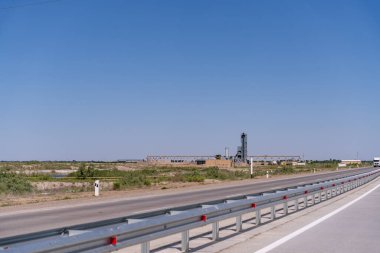 Uzakta yüksek bir binası olan uzun, boş bir yol. Gökyüzü açık ve mavi