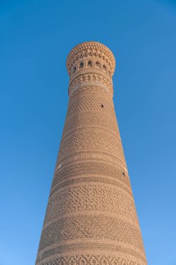 Arka planda mavi gökyüzü olan uzun bir tuğla kule. Kule çok uzun ve eşsiz bir tasarımı var.
