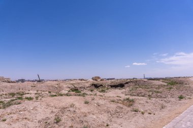 Arka planda mavi gökyüzü olan çorak bir çöl manzarası. Gökyüzü açık ve parlak ve görünürde hiç bulut yok.