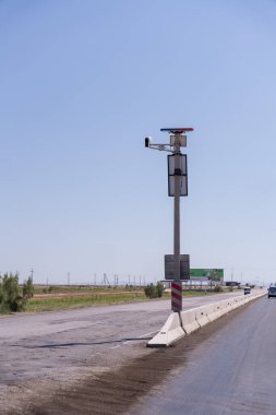 Üzerinde işaret olan bir direk ve üzerine bir kamera monte edilmiş. Direk yolda ve gökyüzü mavi.