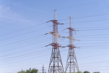 Üzerlerinde kablolar sallanan iki uzun elektrik direği. Gökyüzü açık ve mavi. Güç hatları güçlü ve iyi korunduğu için istikrar ve güvenilirlik kavramı