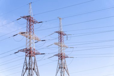 Gökyüzünde iki uzun elektrik hattı var, biri kırmızı ve beyaz. Gökyüzü açık ve mavi