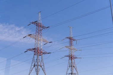 Gökyüzünde iki uzun elektrik hattı var, biri kırmızı ve beyaz. Gökyüzü açık ve mavi