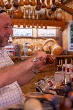 Bir adam dükkanda içki yapıyor. Dükkan vazolar ve şişeler de dahil olmak üzere çeşitli eşyalarla dolu.