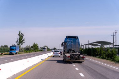 Önünde bir araba olan mavi bir kamyonet otobanda ilerliyor. Gökyüzü açık ve yol boş.