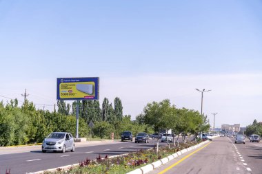 Bir ürünün reklamını yapan yol kenarındaki reklam panosu. Reklam panosu mavi ve beyaz. Yollar araba ve kamyonlarla dolu.