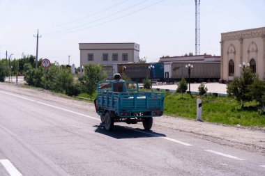 Mavi bir kamyon yolda ilerlerken arkasında kasklı bir adam vardı. Kamyon bir sürü kutu taşıyor.