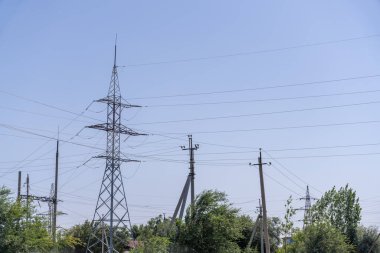 Bir elektrik hattı kulesi ağaçlarla çevrilidir. Gökyüzü açık ve mavi. Güç hatları yüksek ve yayılıyor.