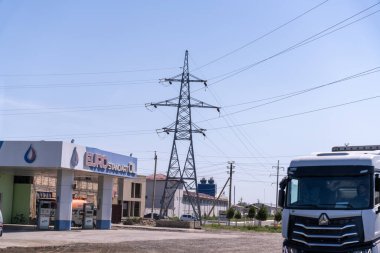 Arkasında büyük bir elektrik hattı olan bir benzin istasyonu. Benzin istasyonunun önünde bir kamyon duruyor.