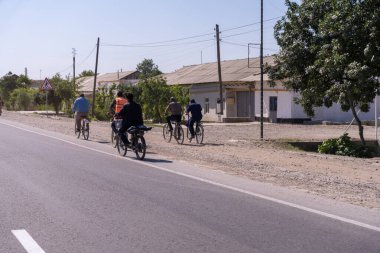 Bir grup insan yolda bisiklete biniyor. Yol boş ve gökyüzü temiz.