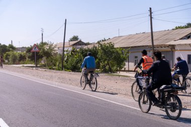Bir grup insan yolun aşağısında bisiklet sürüyor. Binicilerden biri yelek giyiyor.