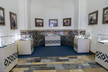 Bir sürü cam kılıfı ve mavi halısı olan bir oda. Oda, birkaç vazo ve birkaç resim de dahil olmak üzere birçok farklı türde eşyayla dolu. Odanın çok temiz ve düzenli bir görünüşü var.