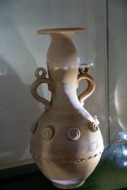 Bir masanın üzerinde spiral desenli kil bir vazo oturuyor. Vazo kahverengi ve eşsiz, sanatsal bir görünüme sahip. Vazodaki tasarım karmaşık ve detaylı, ona zarafet hissi veriyor.