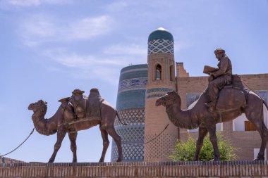 Bir binanın yanındaki duvarda iki deve heykeli var. Develerden biri sırtında bir adam taşıyor.