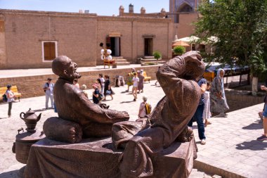 Etrafında bir sürü insan olan bir bankta oturan iki adamın heykeli. Heykel bir erkek ve bir kadının heykeli ve ikisi de yukarı bakıyor.