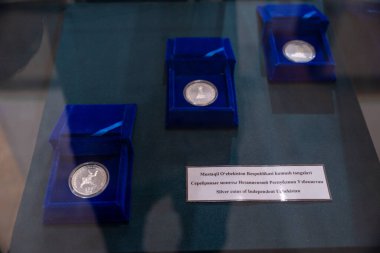 Mavi bir kutuda üç gümüş sikke sergilenir. Kutu cam bir masanın üzerine konur. Bozuk paralar farklı ülkelerden ve farklı tasarımları var.