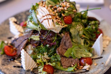 Tabakta et ve sebze olan bir salata. Salata peynir ve fındıkla kaplı.