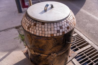 Üstünde kapağı olan büyük metal bir kap. Kapak gümüşten ve kare şeklinde deseni var.