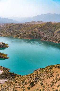 Arkasında dağlar olan güzel bir göl. Su sakin ve berrak. Suda bir tekne yüzüyor.