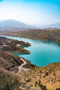 Arka planda mavi gökyüzü olan güzel bir dağ gölü. Göl ağaçlar ve dağlarla çevrili.