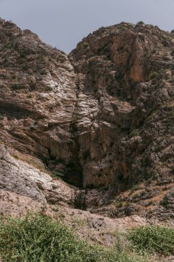 Ortasında büyük bir delik olan bir dağ. Delik kayalar ve otlarla çevrili. Dağ çok uzun ve kayalıktır.