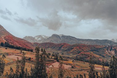 Arka planda bulutlu bir gökyüzü olan bir dağ sırası. Dağlar karla kaplı ve gökyüzü bulutlu.